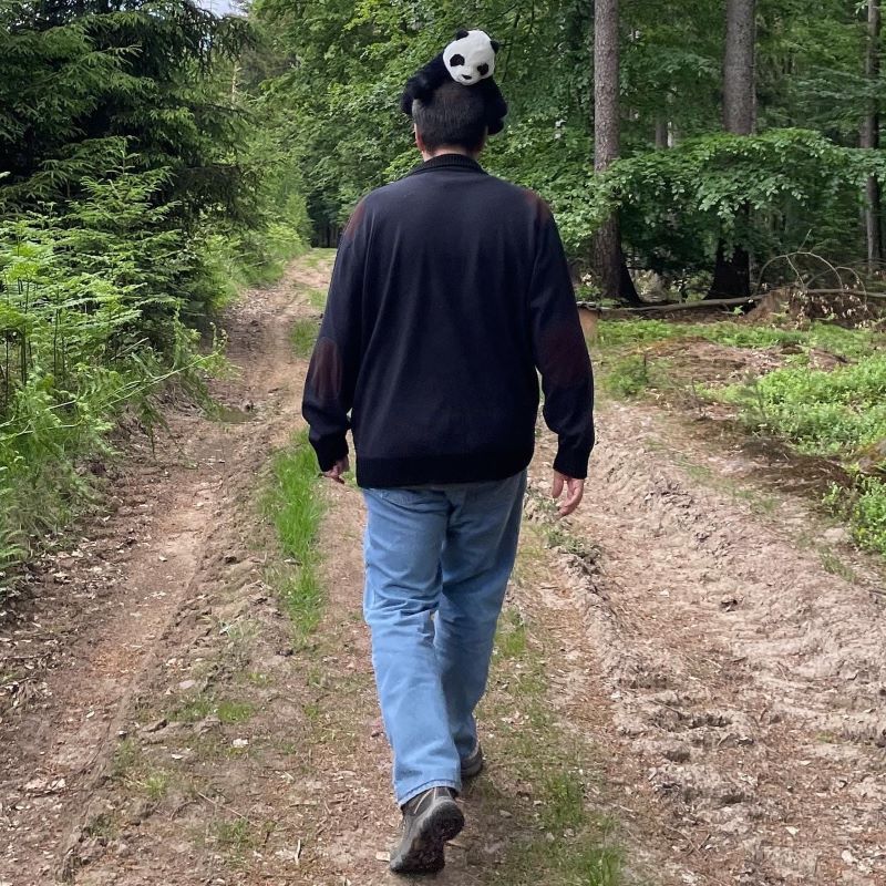 großer Mann geht auf einem Wanderweg und hat einen Plüschpanda auf dem Kopf